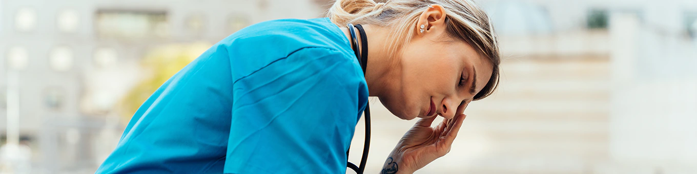 Erschöpfte Pflegehelferin sitzt draußen und hält sich an der Stirn.