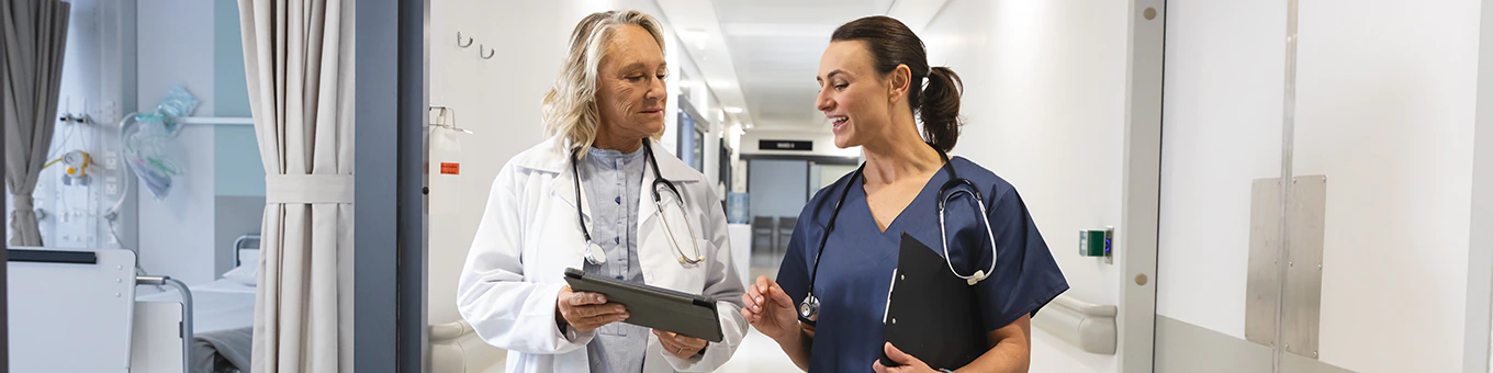 Ärztin und Krankenschwester laufen Gang im Krankenhaus entlang und unterhalten sich.